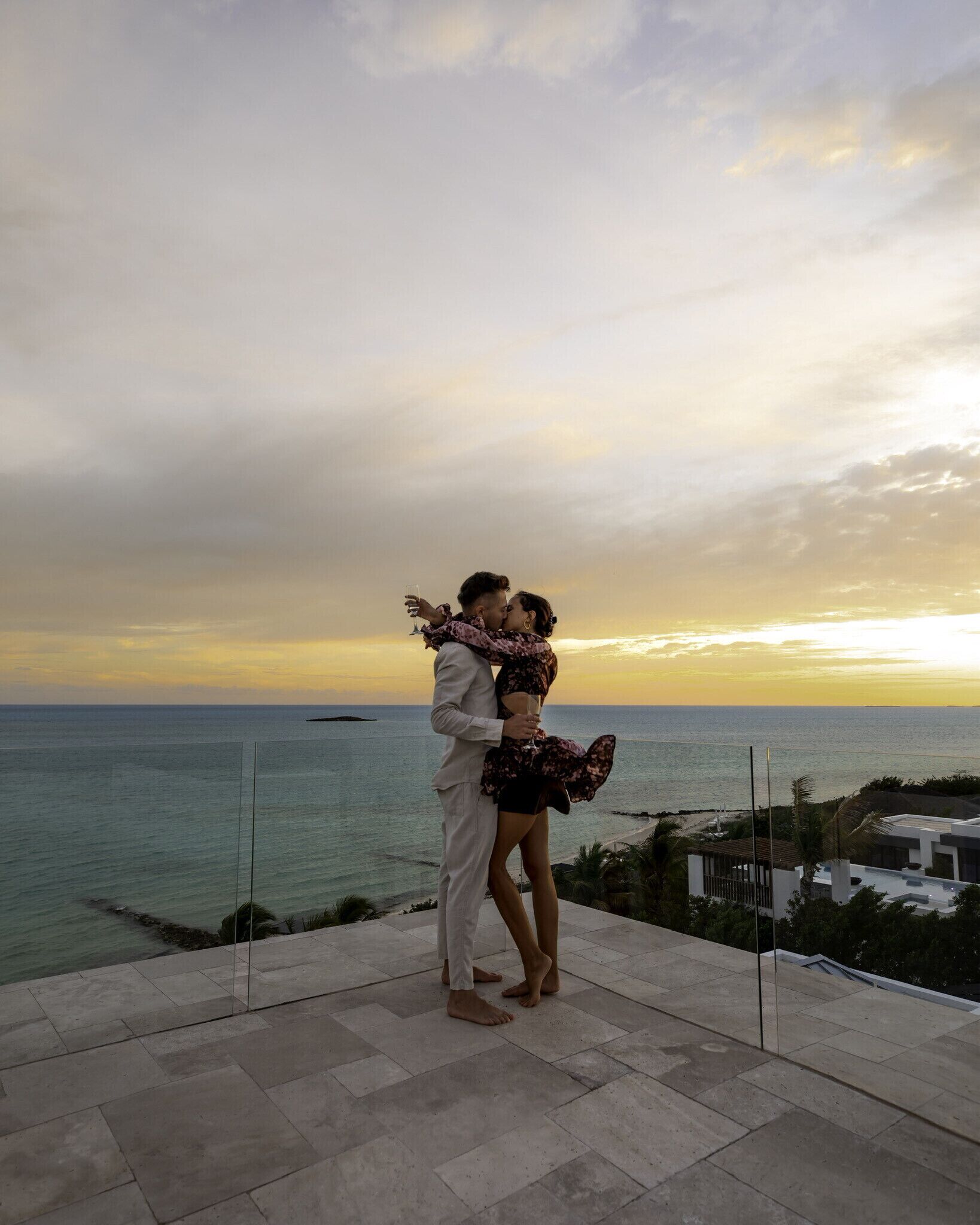 A couple embracing on a terrace overlooking a beach at sunset.