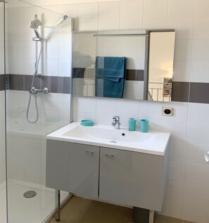 Ein Badezimmer mit einer gläsernen Duschkabine, einem weißen Waschbecken und zwei türkisfarbenen Tassen sowie einem Spiegel über dem Waschbecken.