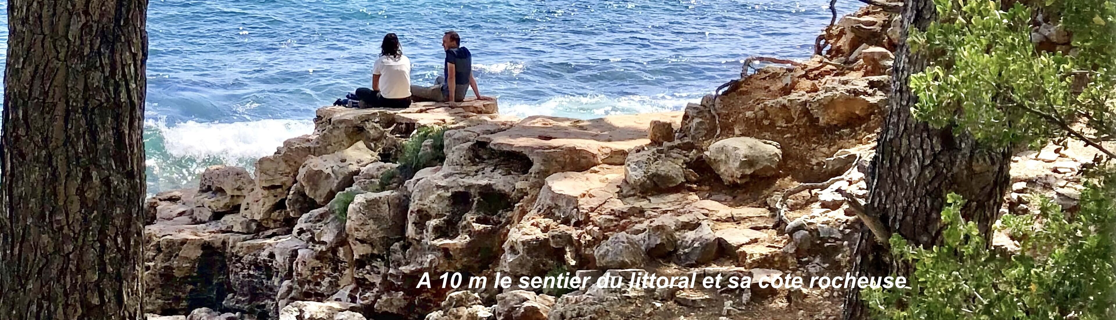 Two people sitting on a rocky outcrop overlooking the sea.