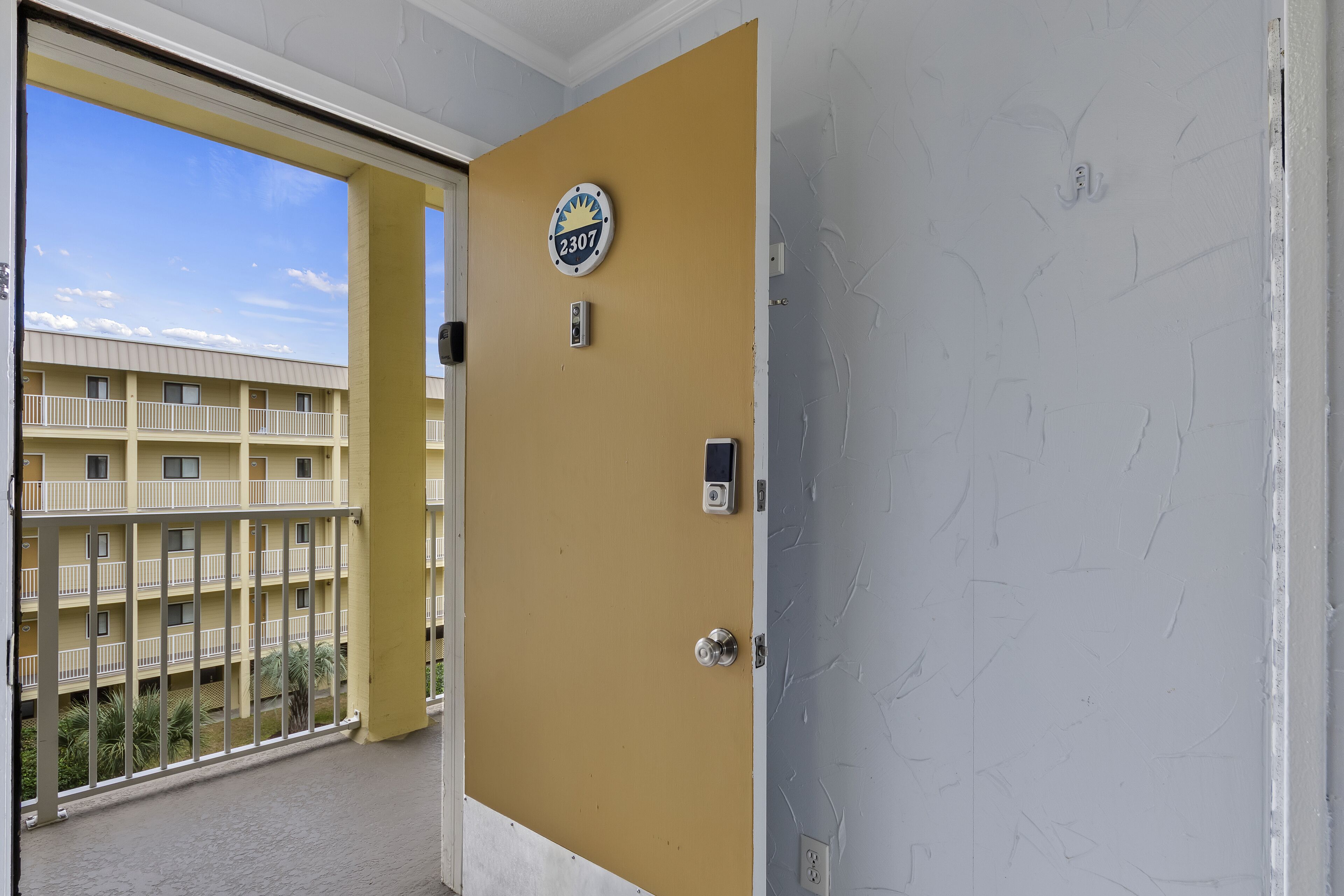 Ein Hotelzimmer mit Balkon, einer Tür mit Nummernschild und Blick auf ein Gebäude mit mehreren Balkonen.