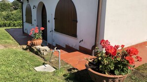 A building with three arched windows, a tiled roof, and a potted plant with red flowers in the foreground.
