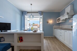 A modern kitchen with white cabinetry, a built-in TV, and a large window with curtains.