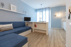 A modern living room with a blue sofa, a flat-screen TV, a desk with a computer, and a window with curtains.