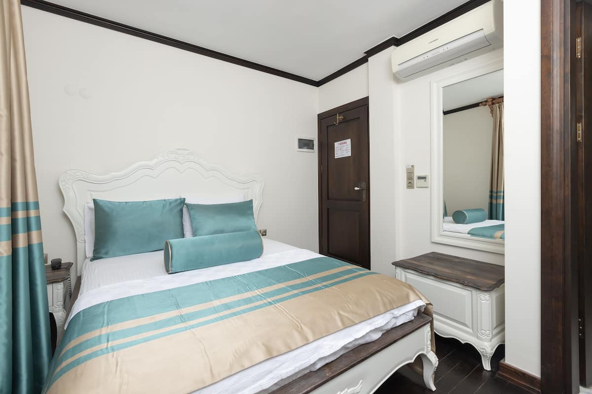 A neatly made bed with a striped bedspread, a wooden nightstand with a lamp, and a mirror above a wooden dresser.