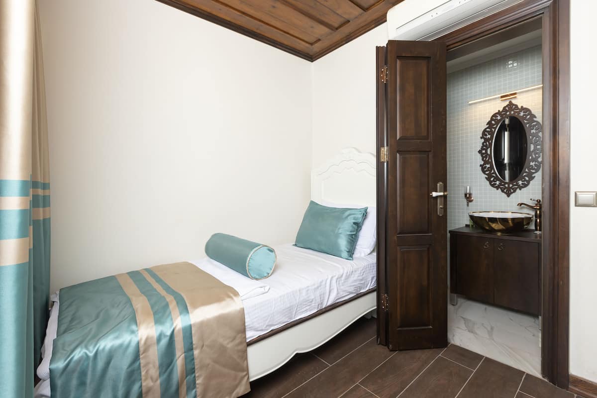 A bedroom with a bed, a bathroom with a sink and mirror, and a wooden door.