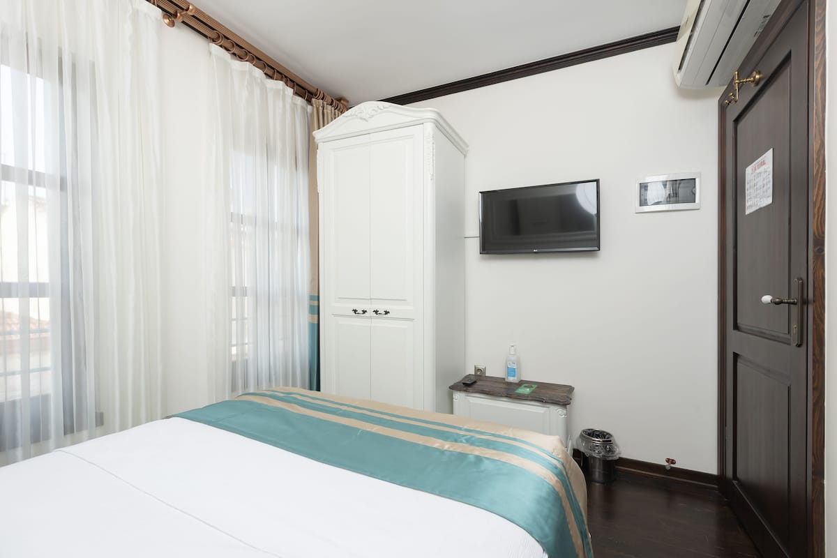 A hotel room with a bed, a wardrobe, a TV, and a small table with a bottle and a remote control.