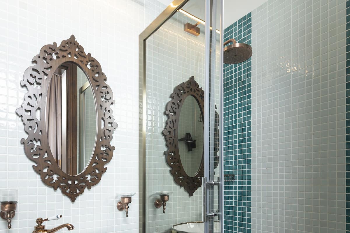 A bathroom with a large oval mirror, a vessel sink, and a glass-enclosed shower.