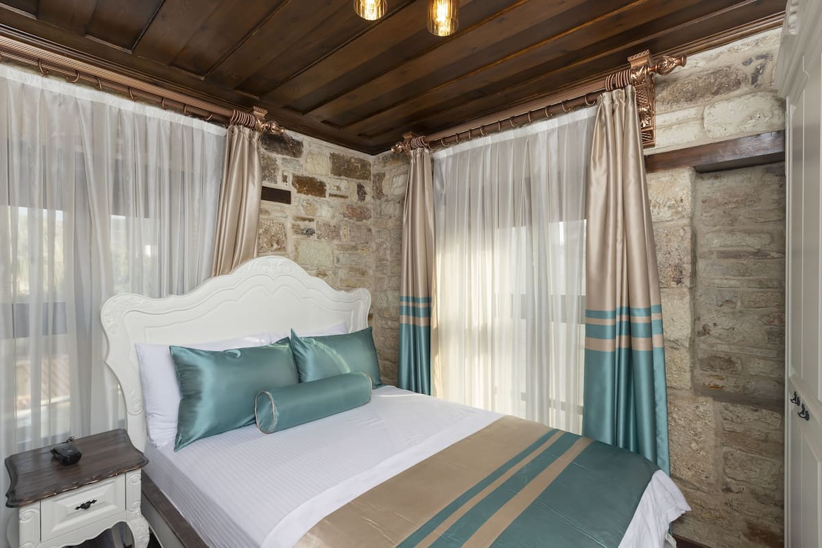 A neatly made bed with a striped bedspread, a white headboard, and teal pillows.