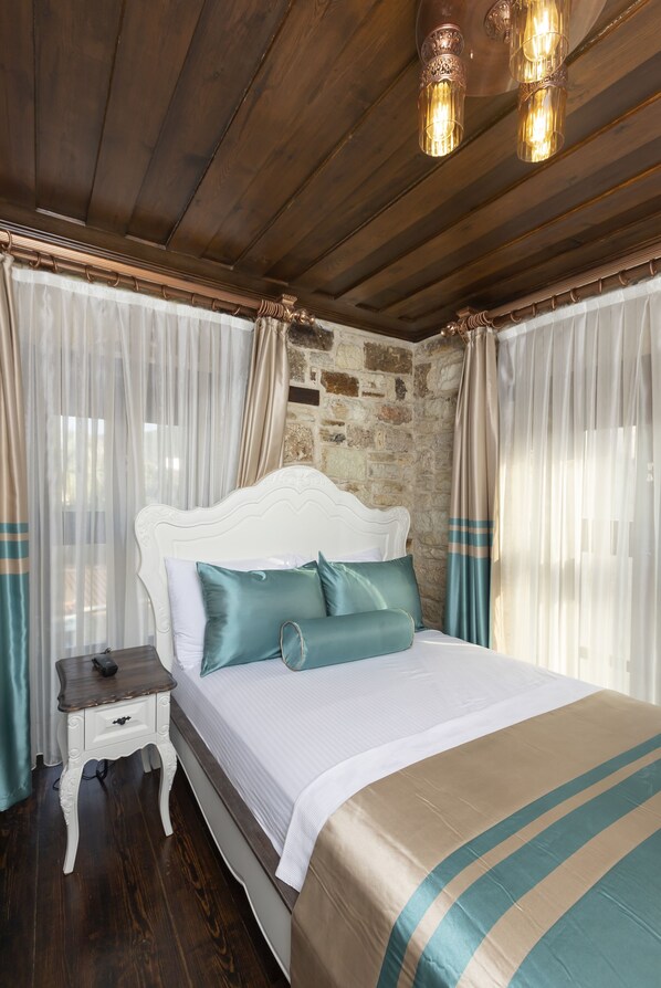 A bedroom with a wooden ceiling, a white bed with teal pillows, a nightstand, and sheer curtains. - Marina Foça Hotel (Foça)