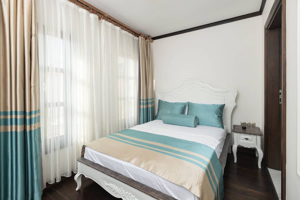 A neatly made bed with a striped bedspread, a bedside table with a lamp, and sheer curtains.