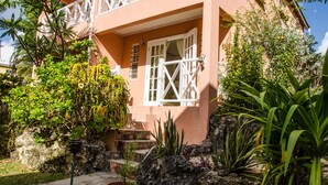 A pink building with white railings, a staircase, and various plants.