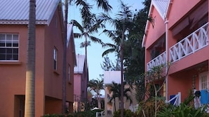 A pathway flanked by buildings with balconies, surrounded by tropical vegetation.
