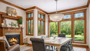 A dining room with a fireplace, large windows, and a chandelier.