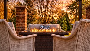 An outdoor seating area with wicker chairs, a fire feature, and a brick wall.