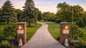 A pathway leading to a gated entrance with a brick wall, a statue, and an American flag.