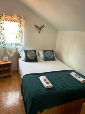 Una cama bien hecha con un edredón verde, dos almohadas decorativas y un cráneo de vaca montado en la pared.