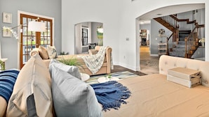 Ein großzügiges Wohnzimmer mit hoher Decke, einer Treppe und Blick in einen weiteren Raum.