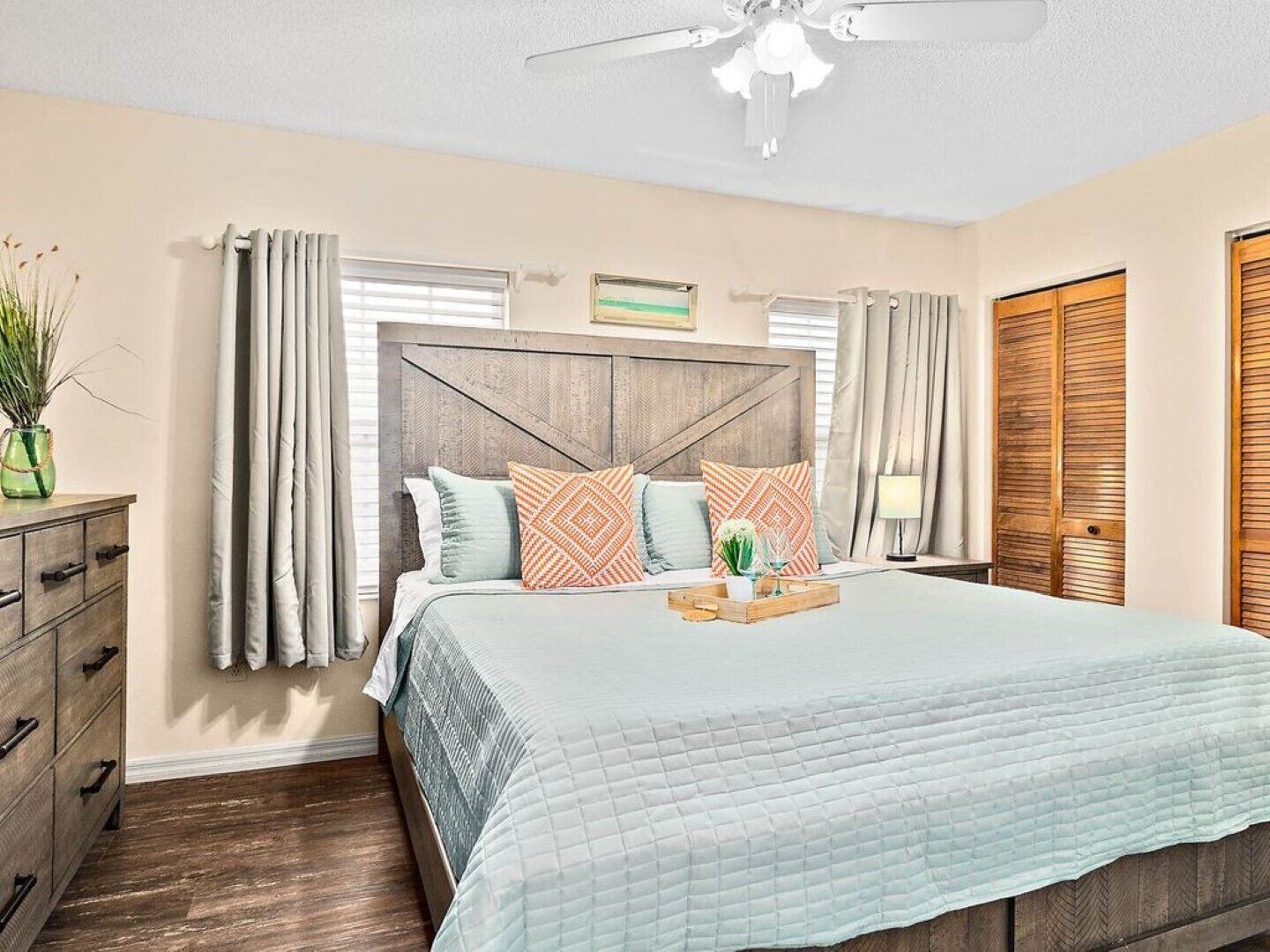 A bedroom with a bed, wooden headboard, curtains, a dresser, and a ceiling fan.