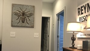 A hallway with a wooden floor, a wall-mounted lamp, and a framed artwork of a bee. - Reynolds Villa- Golf/Couples Retreat (Southern Pines)