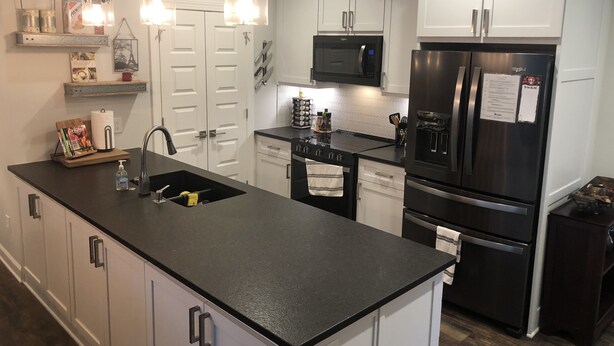 A modern kitchen with white cabinets, a black countertop, stainless steel appliances, and pendant lighting. - Reynolds Villa- Golf/Couples Retreat (Southern Pines)