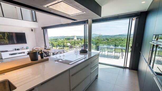 Una cocina moderna con una isla grande, horno empotrado y un ventanal con vistas a un paisaje verde.