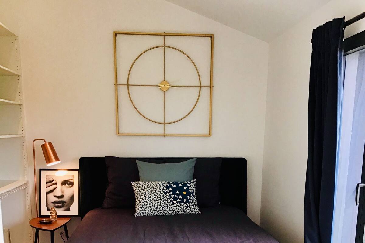 Quarto com cama, tapete, uma obra de arte na parede e janela com cortinas.