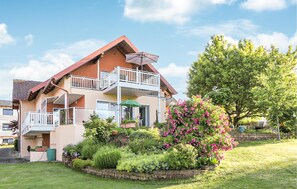 Et toetagers hus med balkon, omgivet af en velplejet have med forskellige planter og blomster.
