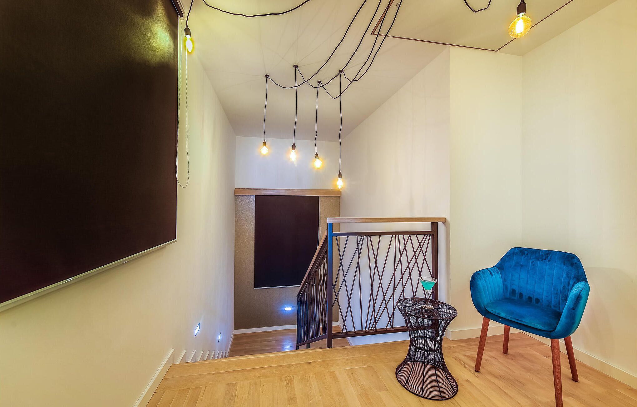 Un interior modern amb una cadira blava, una escala i llums penjants.