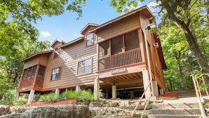 A two-story house with a wooden exterior, a balcony, and a stone staircase leading to the entrance. - "Back-Porch Sittin'" Perfect! Walk-in Cedar Cabin near 76 Country Blvd Strip! (Branson)