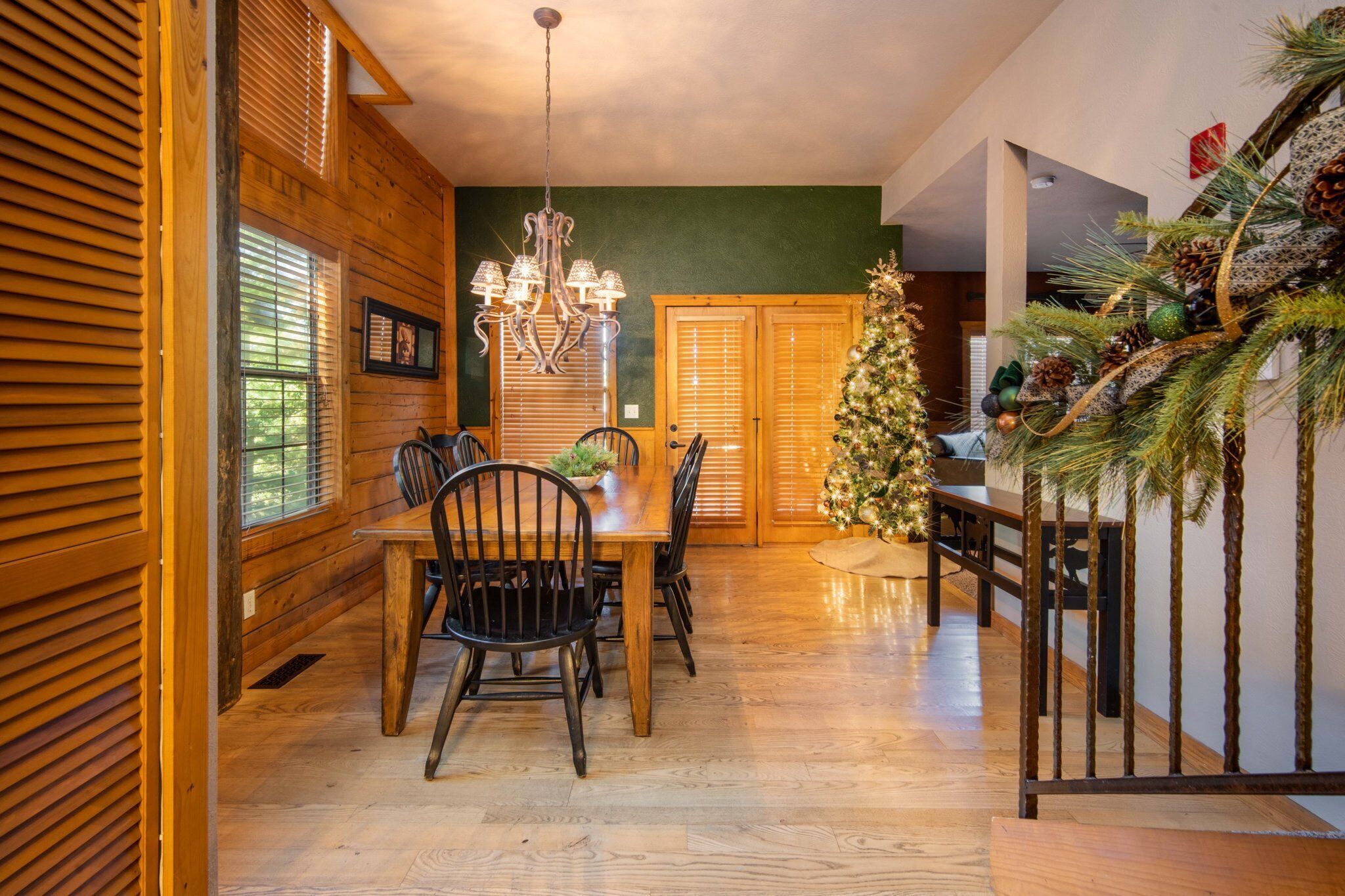 Un comedor con mesa y sillas de madera, una lámpara de araña y un árbol de Navidad.