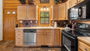 A kitchen with wooden cabinets, a dishwasher, a stove, and a microwave. - "Back-Porch Sittin'" Perfect! Walk-in Cedar Cabin near 76 Country Blvd Strip! (Branson)
