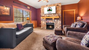 A cozy living room with a stone fireplace, a ceiling fan, and a large window with blinds. - "Back-Porch Sittin'" Perfect! Walk-in Cedar Cabin near 76 Country Blvd Strip! (Branson)
