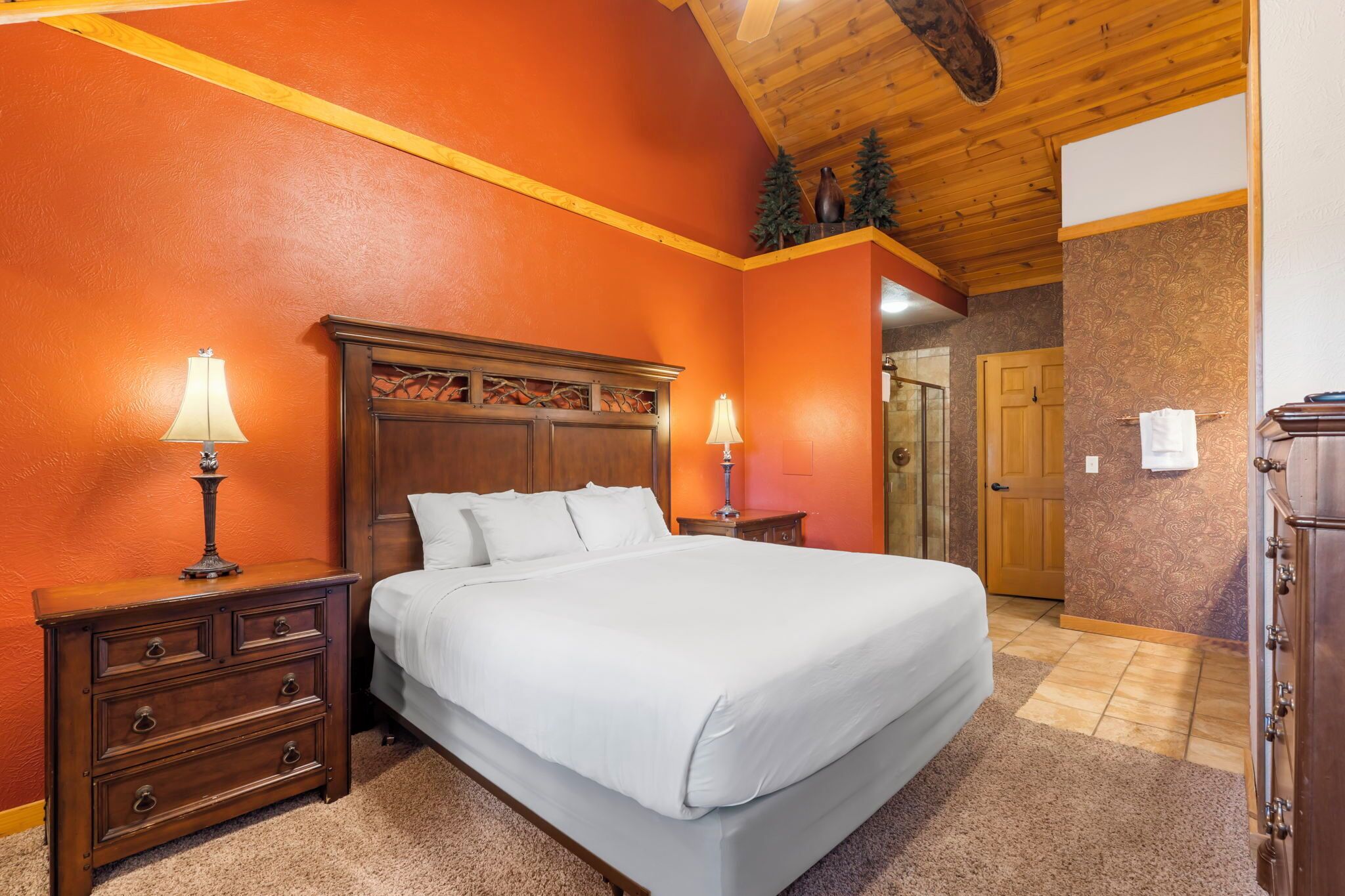 Un dormitorio con una cama de madera, dos mesitas de noche con lámparas, un aparador y una puerta que da a otra habitación.