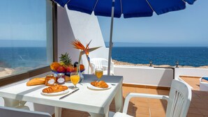A table with breakfast items, a view of the sea, and a blue umbrella. - Reyes Natur - Bungalow on the seafront (Charco del Palo)