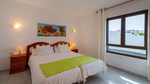A hotel room with a bed, two bedside tables, a nightstand, a painting on the wall, and a window with a view. - Reyes Natur - Bungalow on the seafront (Charco del Palo)