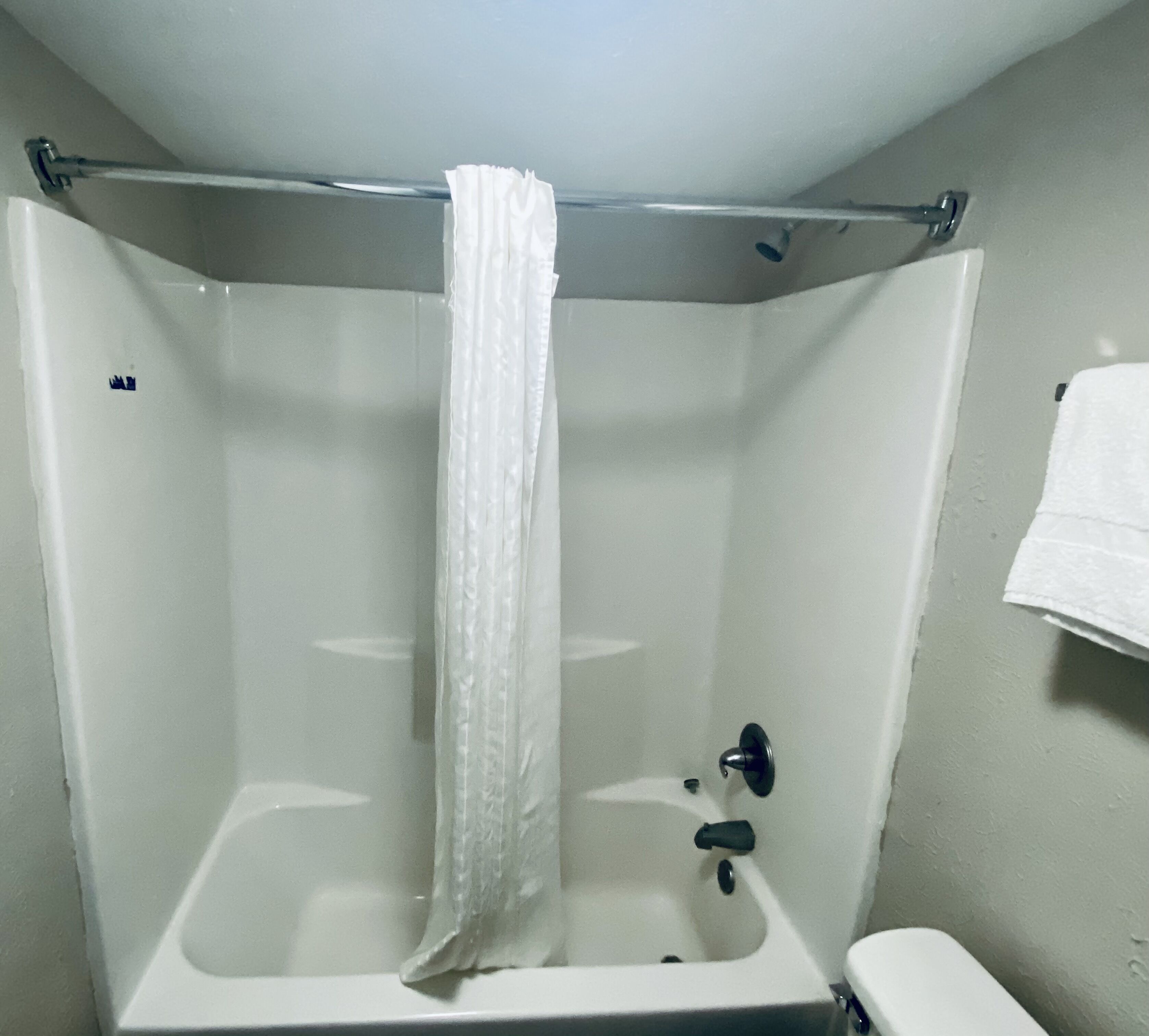 A corner shower with a white curtain, a handheld showerhead, and a towel rack on the wall.
