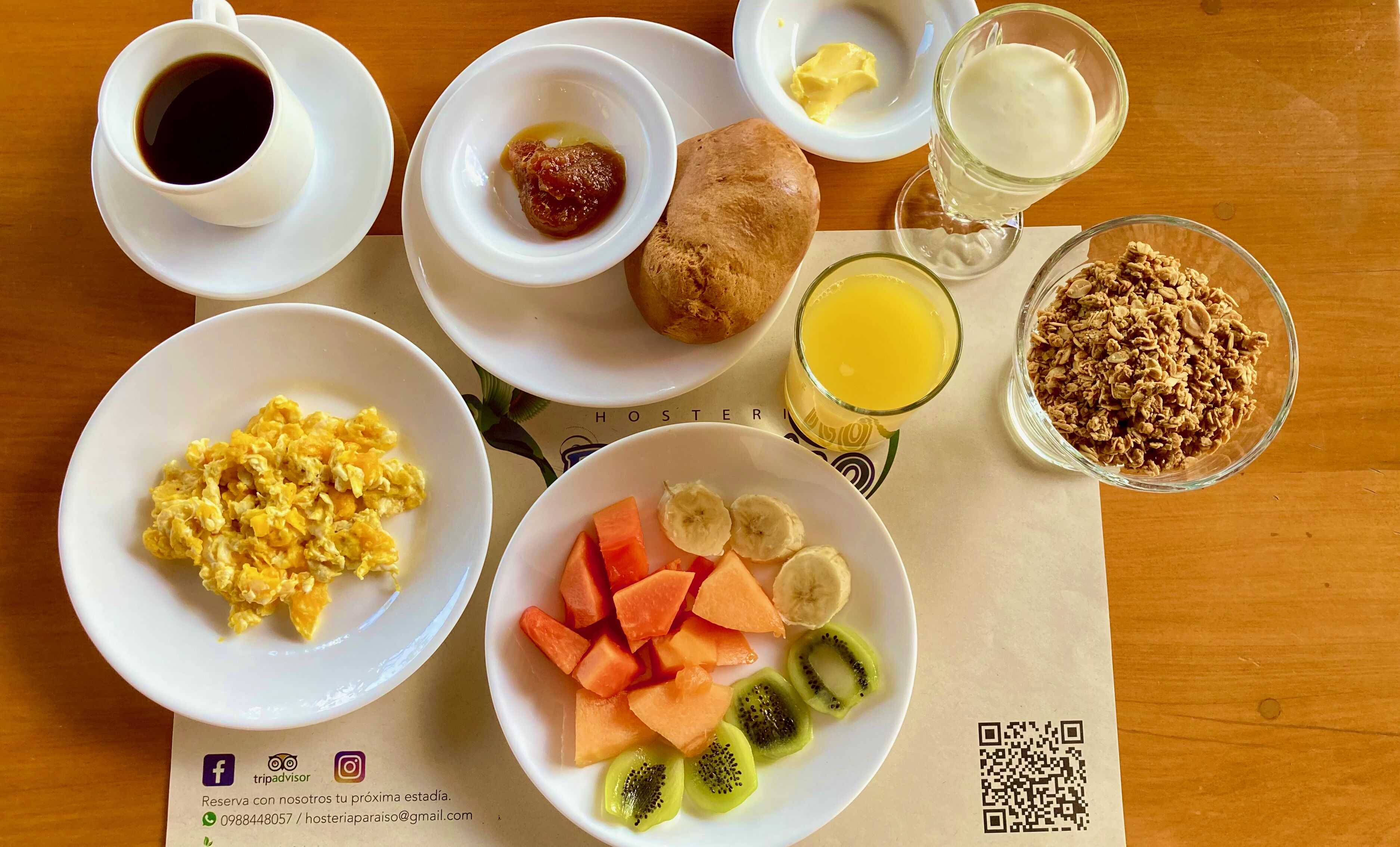A breakfast table with scrambled eggs, fruit, toast, butter, and juice.