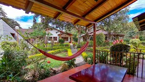 A hammock under a wooden pergola, a brick patio, and a well-maintained garden with various plants and a pathway. - Hostería Paraíso (Vilcabamba)