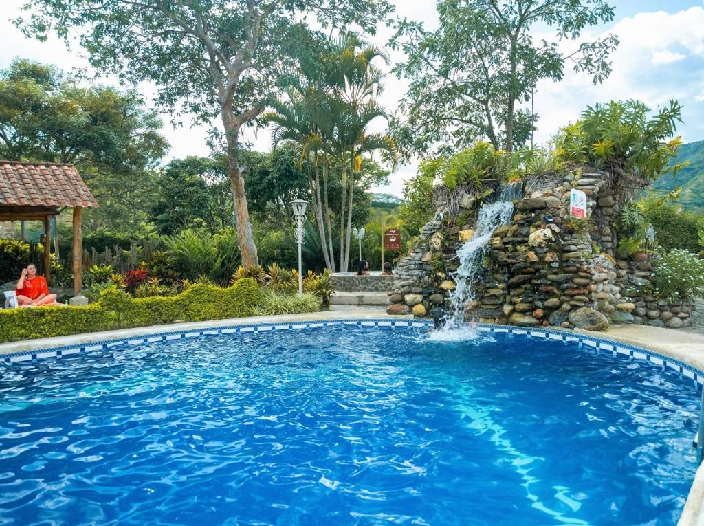 A swimming pool with a waterfall feature, surrounded by lush greenery and a gazebo.