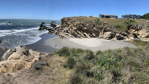 A coastal landscape with rocky terrain, a sandy beach, and a clear blue sky.