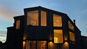 A modern two-story house with large windows and a covered outdoor seating area.
