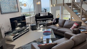 A spacious living room with a large TV, a piano, and a comfortable sofa.