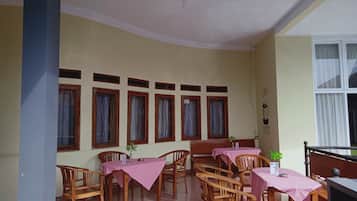 A dining area with wooden chairs and tables, a ceiling fan, and a window with curtains.