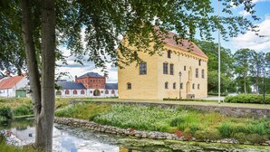 Ein historisches Gebäude mit gelber Fassade und rotem Dach, umgeben von einem Teich und Grünflächen.