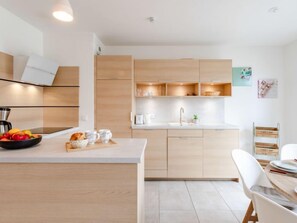 Cozinha moderna com armários de madeira, bancada branca e área de refeições com mesa e cadeiras brancas.