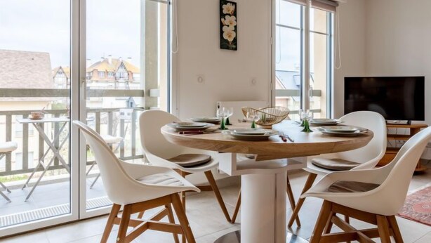 Ein Essbereich mit einem runden Tisch, weißen Stühlen und einem Fernseher im Hintergrund.