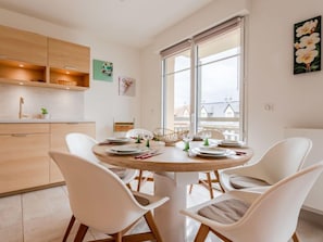 A modern kitchen with white cabinets, a dining table set for four, and a large window with a view of buildings.