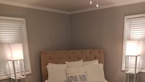 A bedroom with a tufted headboard, a bed with white linens, two bedside lamps, and a bedside table.