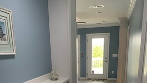 A hallway with a white built-in bench, a door leading to a balcony, and a light-colored wooden floor. - Donovan's Out of the Blue  Great Value and Location! (Oak Island)