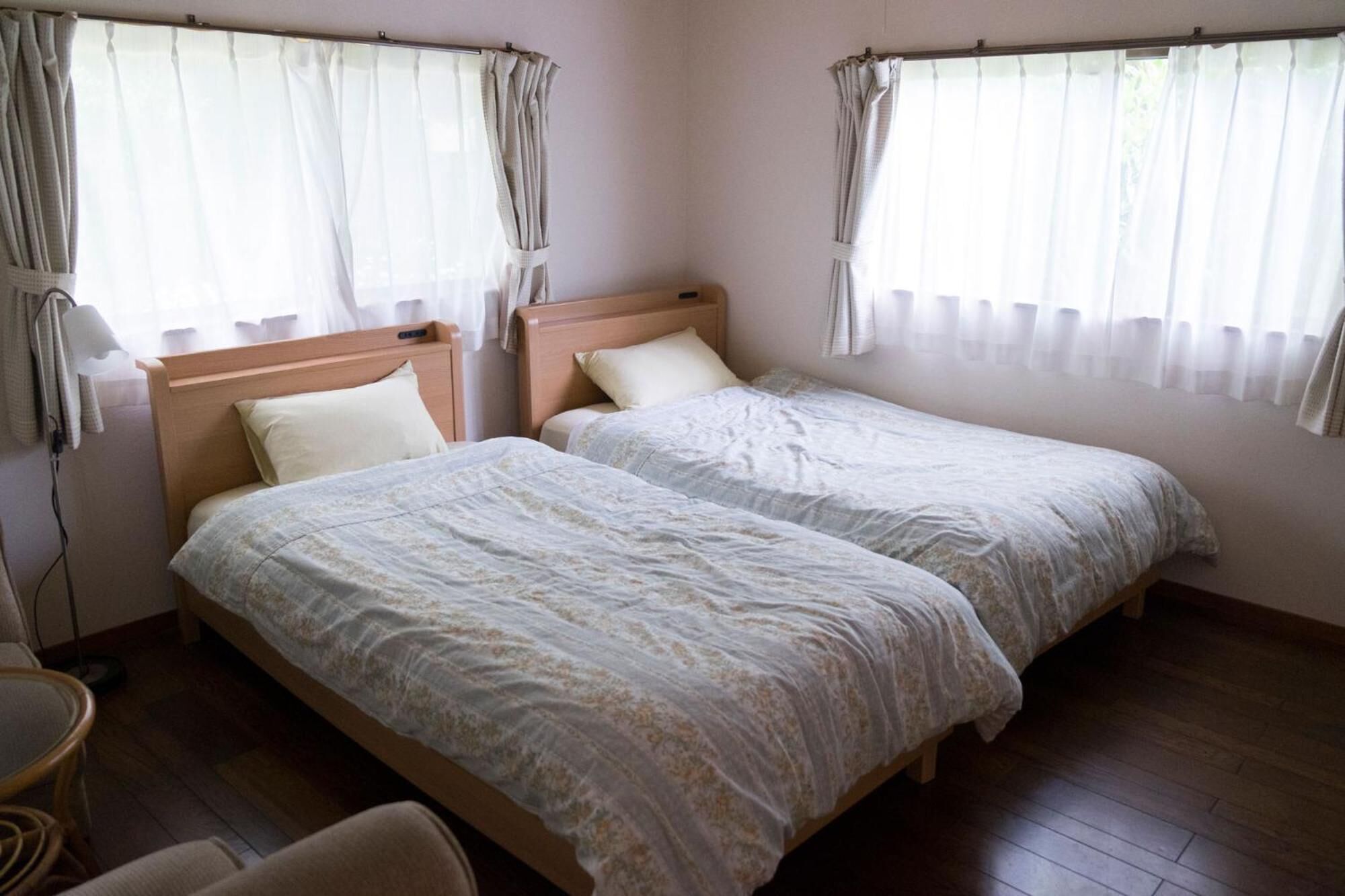 A room with two single beds, a wooden headboard, a small round table, and a chair.
